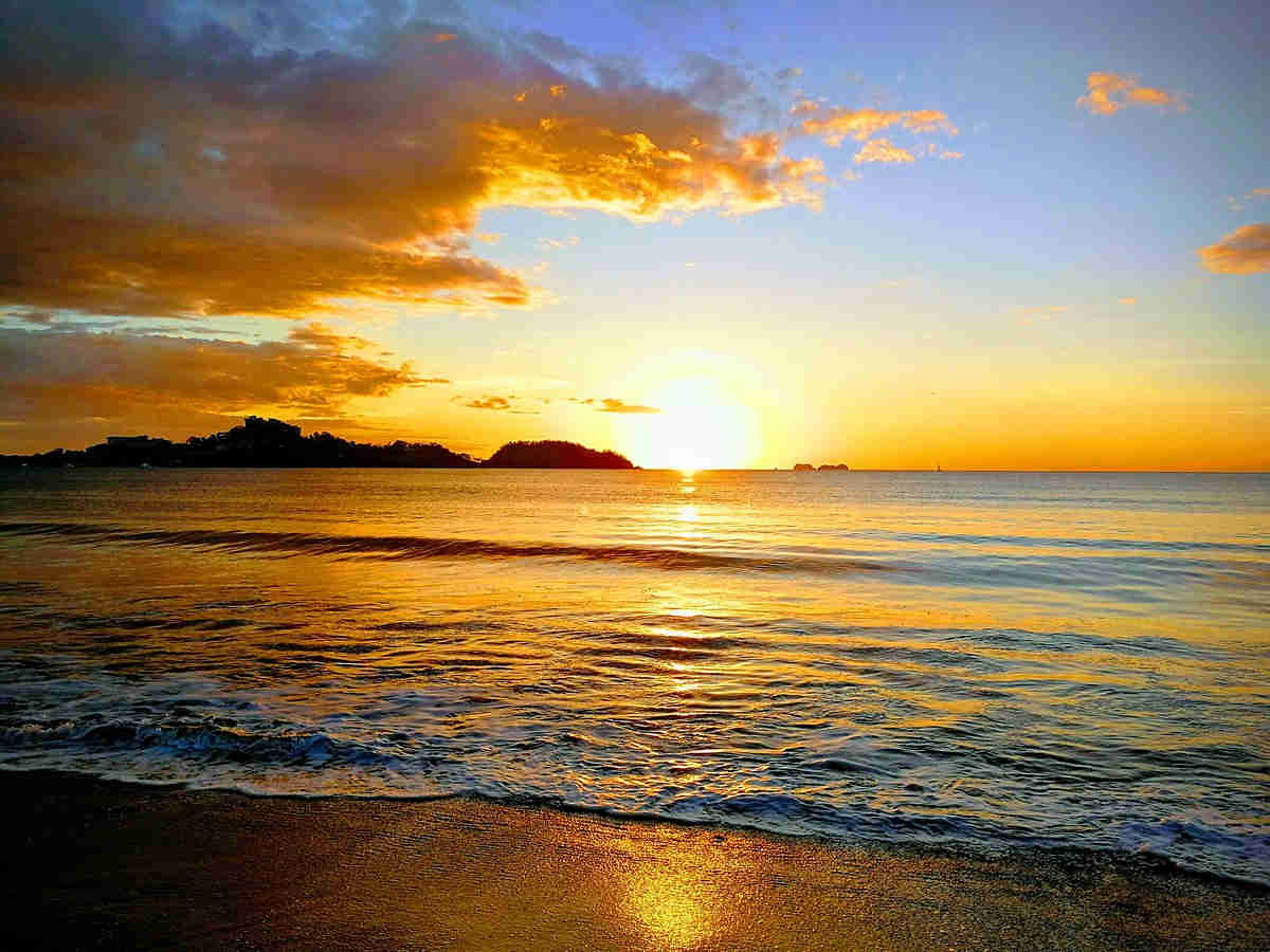 Playa Potrero view from the beach at sunset, colorful cloud and sky with reflective water and sand below