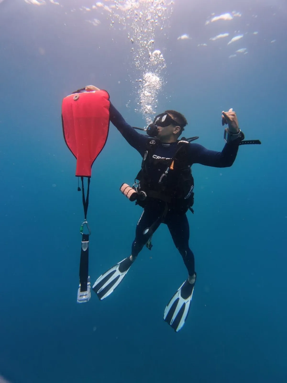 Scuba diver deploying a red delayed surface marker buoy underwater off Playa Potrero, Costa Rica