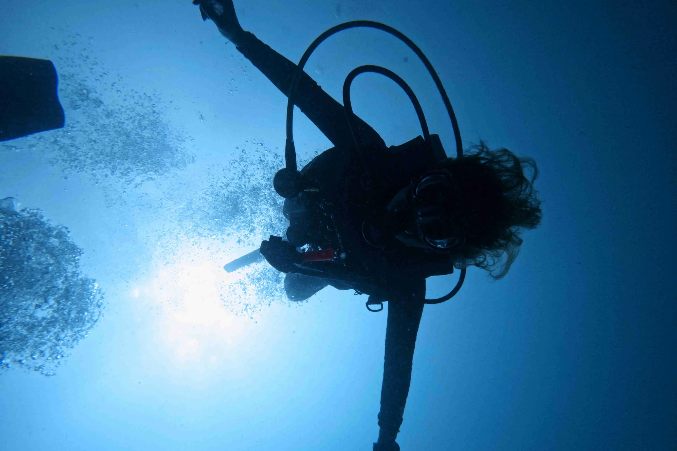 Scuba diver silhouetted against sunlight while descending in deep blue water off Playa Potrero, Costa Rica