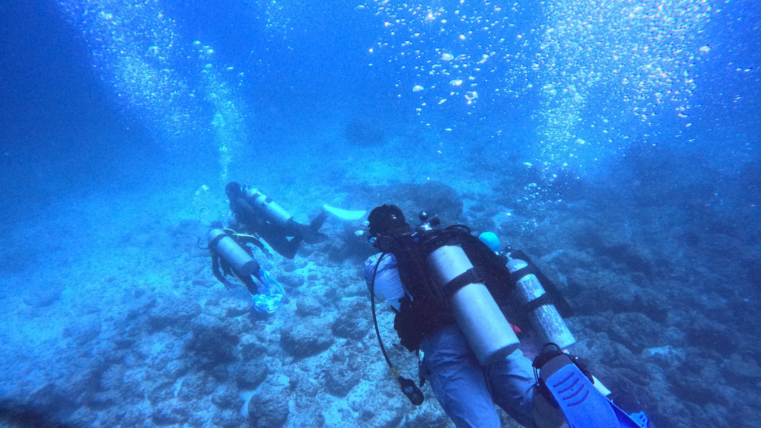 Two scuba divers exploring a rocky reef with bubbles rising toward the sunlit surface off the Guanacaste coast, Costa Rica