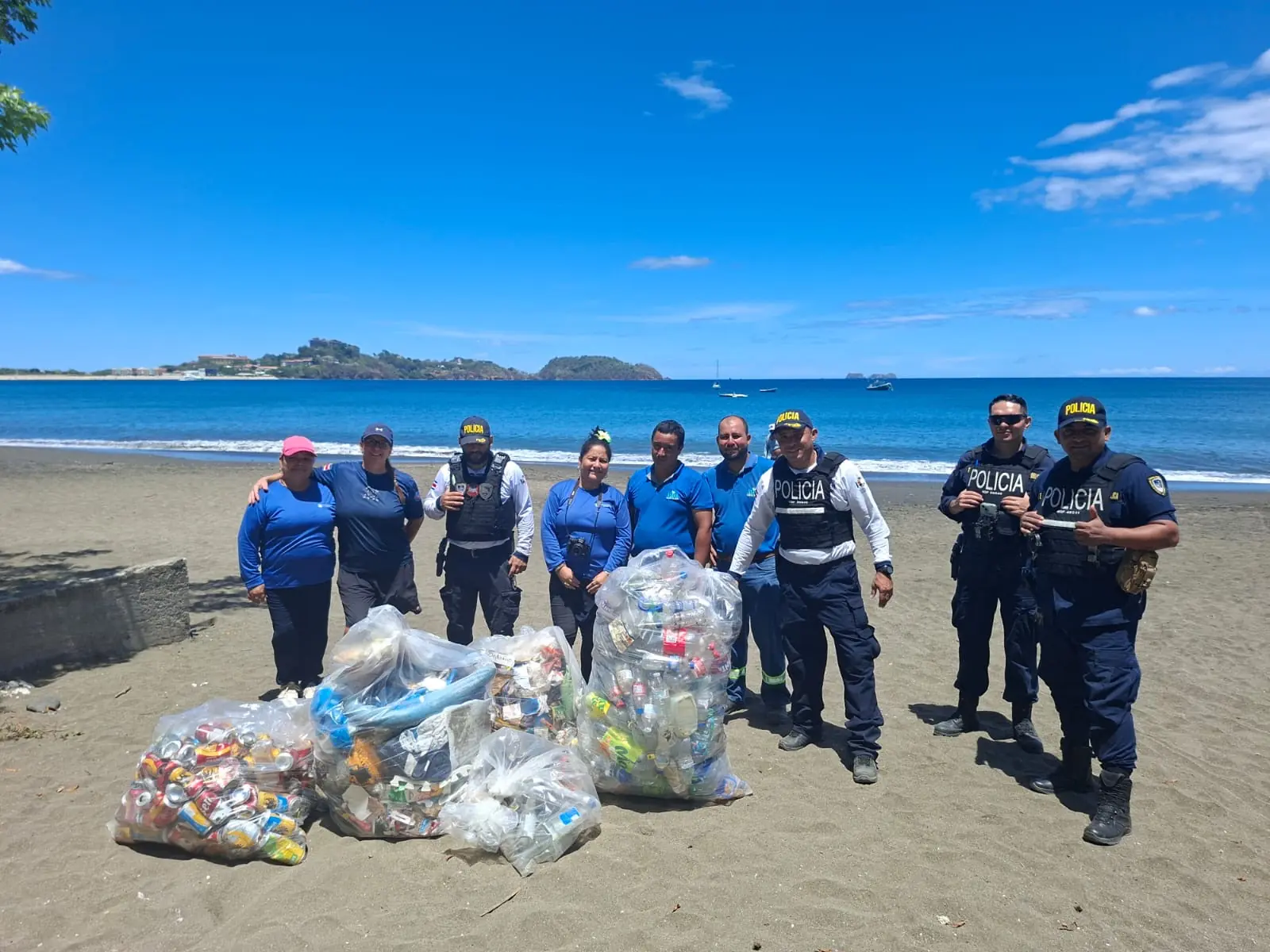Under The Sea Diving crew and Fuerza Pública officers with bags of collected trash at a Playa Potrero beach cleanup, Costa Rica
